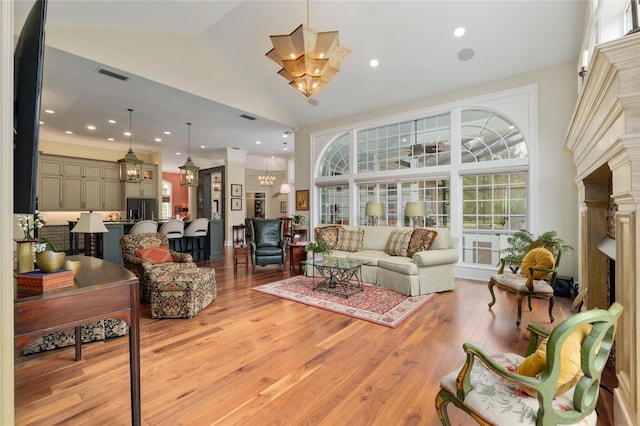 living room featuring light wood-style floors, visible vents, high vaulted ceiling, and an inviting chandelier