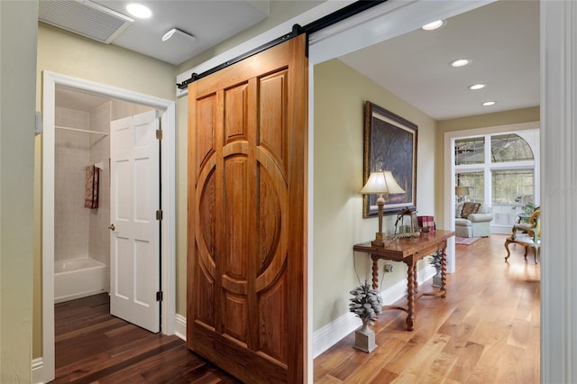 hall with a barn door, recessed lighting, wood finished floors, and baseboards