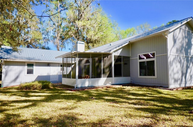 rear view of property with metal roof, a lawn, a chimney, and a sunroom