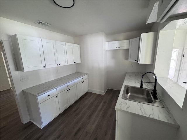 kitchen with a sink, visible vents, baseboards, white cabinetry, and dark wood-style floors