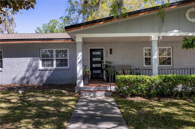 doorway to property with brick siding, covered porch, and a lawn