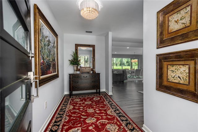 hallway with visible vents, wood finished floors, baseboards, and a chandelier