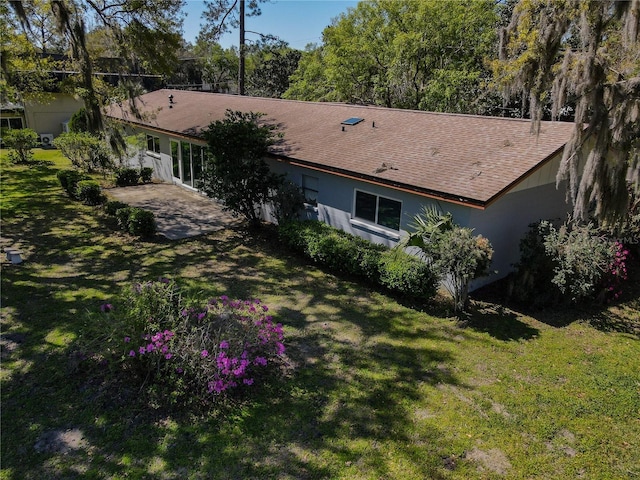 back of house featuring a yard, a shingled roof, stucco siding, and a patio area