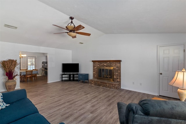 living area featuring visible vents, wood finished floors, vaulted ceiling, a brick fireplace, and ceiling fan with notable chandelier