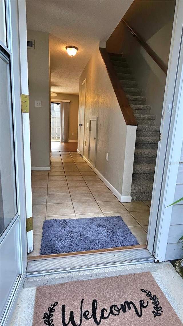 hall with visible vents, a textured ceiling, tile patterned flooring, baseboards, and stairs