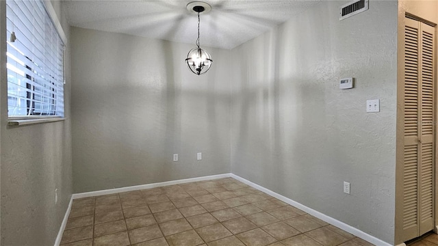 unfurnished dining area with visible vents, a textured wall, a chandelier, tile patterned flooring, and baseboards