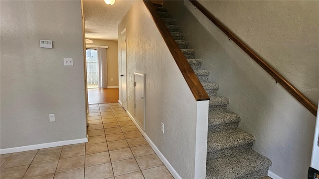 stairs featuring baseboards, a textured wall, a textured ceiling, and tile patterned floors