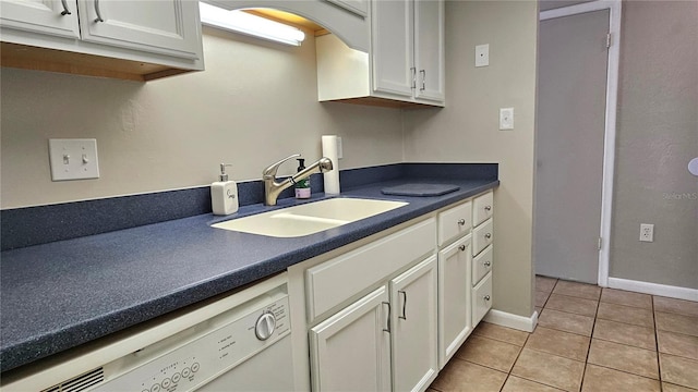 kitchen featuring light tile patterned floors, dark countertops, white dishwasher, and a sink