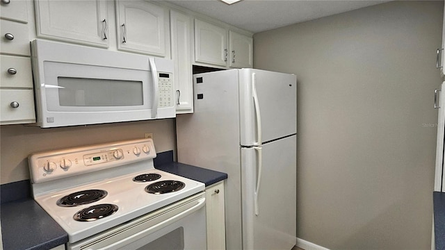 kitchen featuring white appliances, dark countertops, and white cabinetry