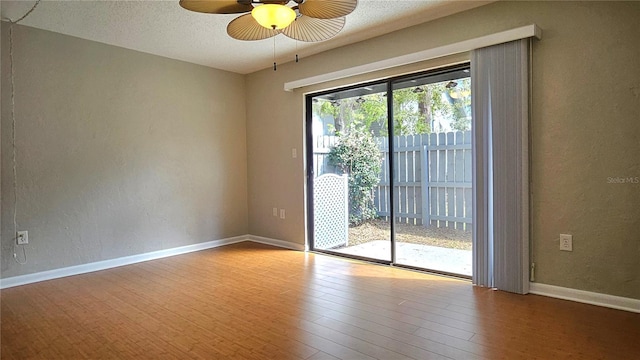 spare room with a textured ceiling, a textured wall, wood finished floors, a ceiling fan, and baseboards