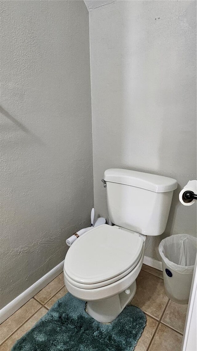 bathroom with toilet, tile patterned flooring, baseboards, and a textured wall