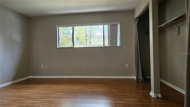 unfurnished bedroom with a textured ceiling, baseboards, and wood finished floors