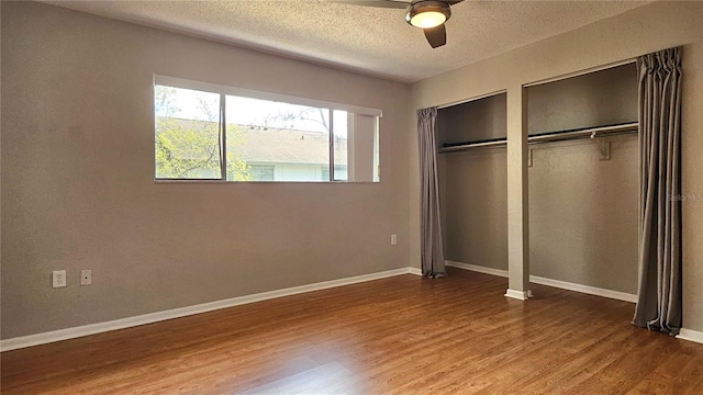 unfurnished bedroom with multiple closets, baseboards, and wood finished floors