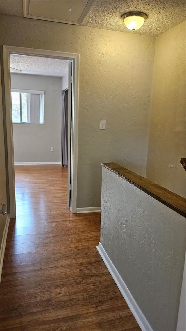 corridor featuring attic access, baseboards, dark wood finished floors, a textured wall, and a textured ceiling