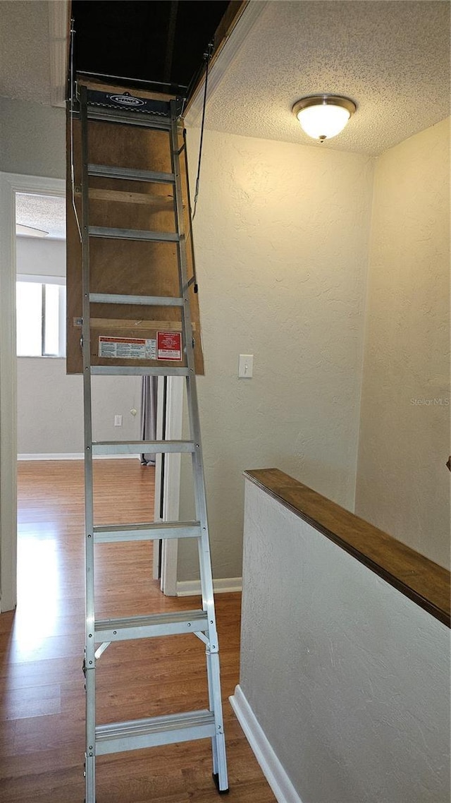 stairs with a textured ceiling, a textured wall, wood finished floors, and baseboards