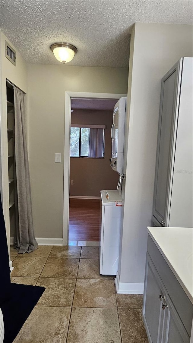 interior space with baseboards, visible vents, stacked washer / drying machine, a textured ceiling, and vanity