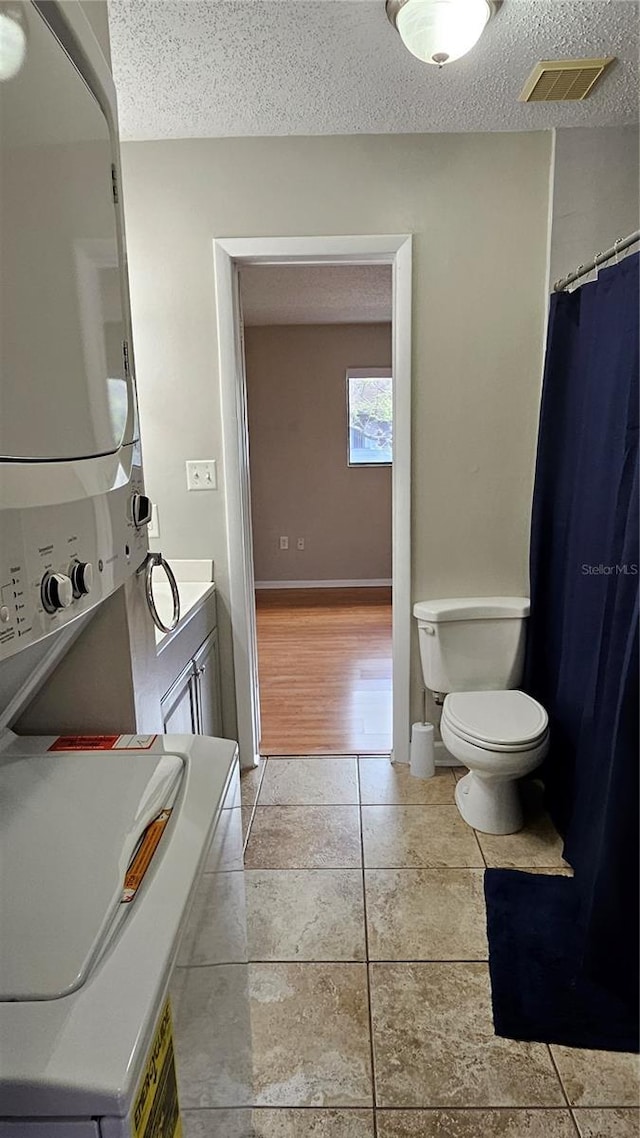 bathroom featuring visible vents, stacked washer / dryer, toilet, tile patterned floors, and a textured ceiling