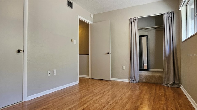 unfurnished bedroom with a textured ceiling, wood finished floors, visible vents, and baseboards