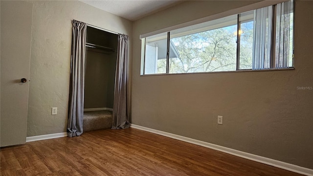 unfurnished bedroom featuring a textured wall, a closet, wood finished floors, and baseboards