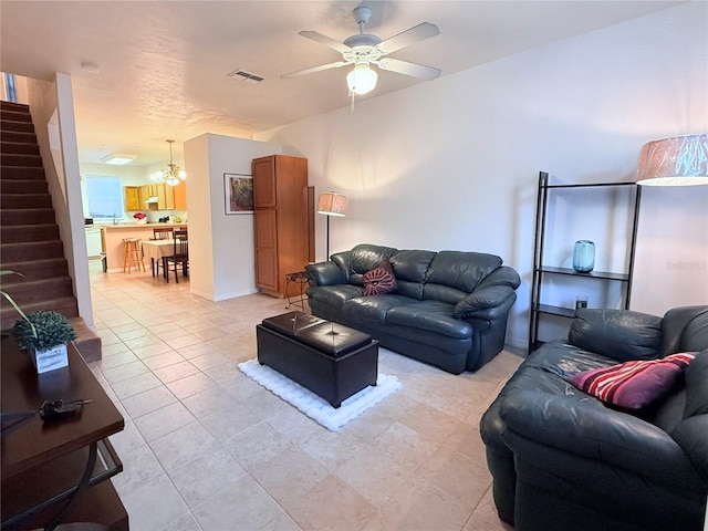 living area with light tile patterned floors, visible vents, stairway, and ceiling fan with notable chandelier