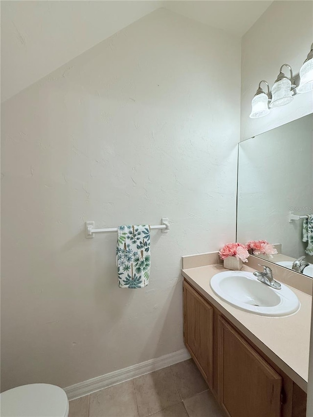 half bathroom with lofted ceiling, toilet, vanity, baseboards, and tile patterned floors