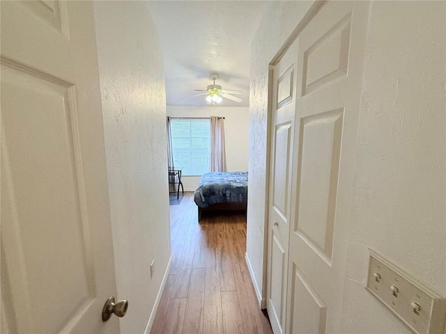 hall featuring a textured wall, baseboards, and wood finished floors