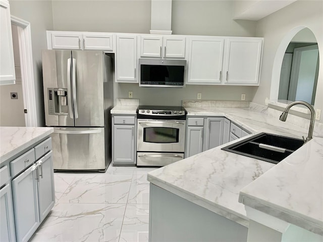 kitchen featuring light stone counters, marble finish floor, stainless steel appliances, gray cabinets, and a sink