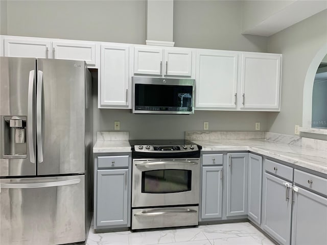 kitchen with marble finish floor, gray cabinets, appliances with stainless steel finishes, white cabinets, and light stone countertops