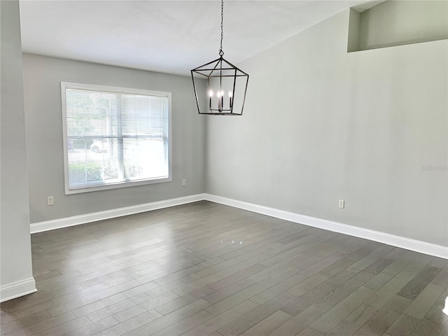 spare room featuring a chandelier, dark wood finished floors, and baseboards