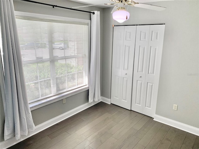 unfurnished bedroom featuring ceiling fan, a closet, baseboards, and dark wood-type flooring