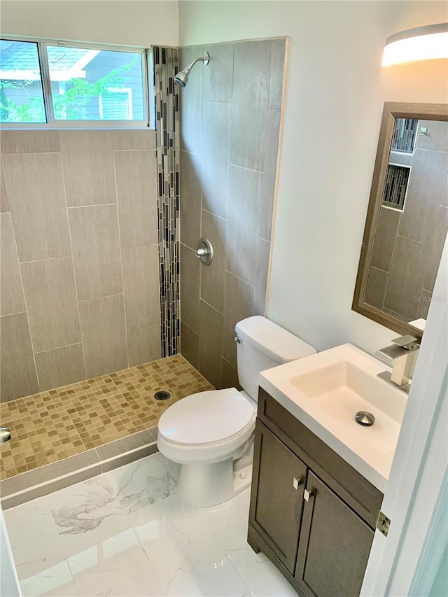 full bathroom featuring toilet, marble finish floor, a tile shower, and vanity