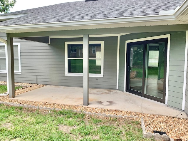 entrance to property featuring a patio and roof with shingles