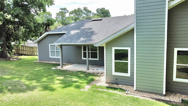 rear view of property with a patio area, roof with shingles, a lawn, and fence