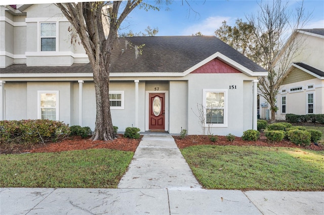 view of front of property featuring a front yard, roof with shingles, and stucco siding