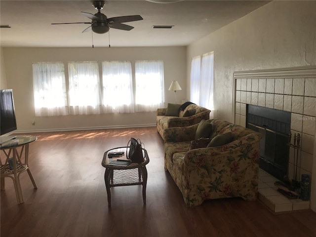 living area with visible vents, a tiled fireplace, a ceiling fan, wood finished floors, and baseboards