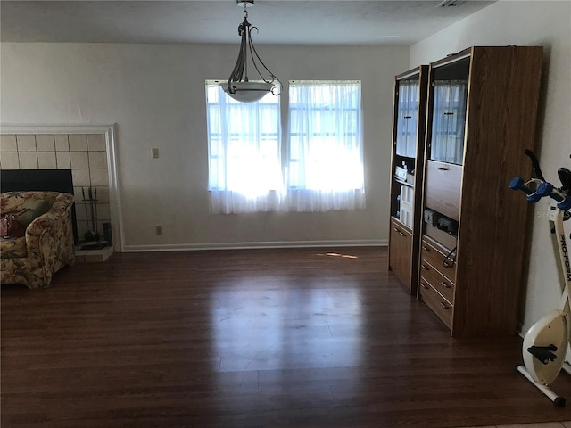 dining space featuring dark wood-type flooring, a tile fireplace, and baseboards