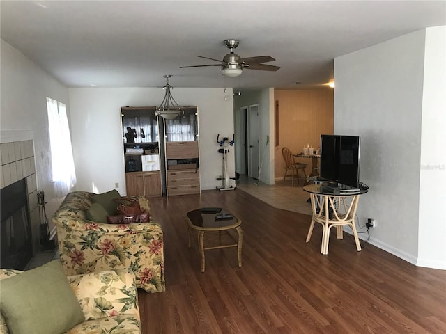 living area featuring a tile fireplace, ceiling fan, baseboards, and wood finished floors