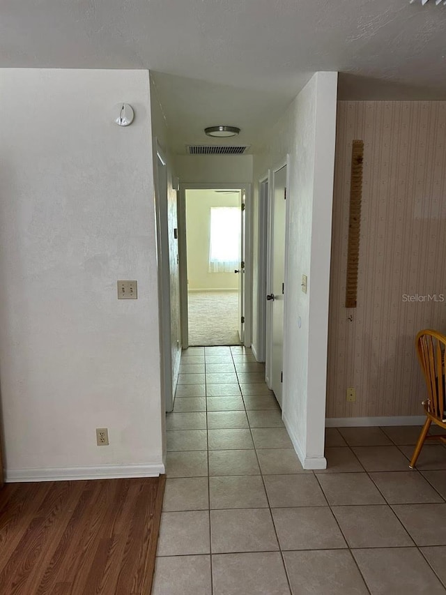 hall with visible vents, baseboards, and light tile patterned flooring