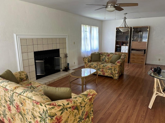 living area with a tiled fireplace, wood finished floors, baseboards, and a ceiling fan