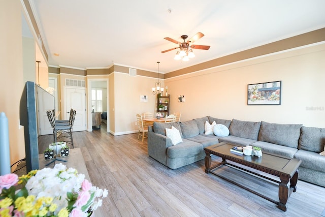 living room featuring crown molding, visible vents, light wood-style floors, baseboards, and ceiling fan with notable chandelier