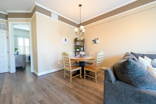 dining space with crown molding, visible vents, an inviting chandelier, wood finished floors, and baseboards