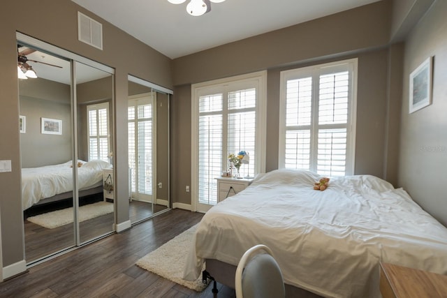 bedroom featuring dark wood-style floors, two closets, visible vents, and baseboards