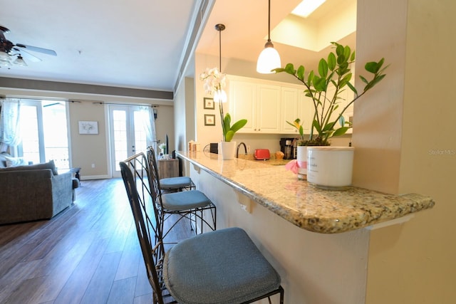 kitchen featuring hanging light fixtures, open floor plan, white cabinetry, wood finished floors, and a kitchen bar