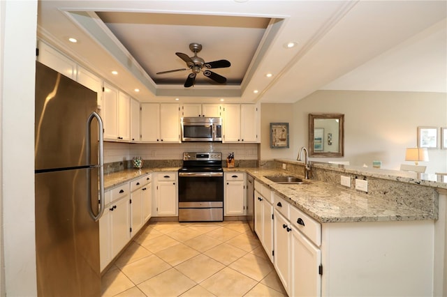 kitchen with stainless steel appliances, a raised ceiling, white cabinetry, a sink, and a peninsula