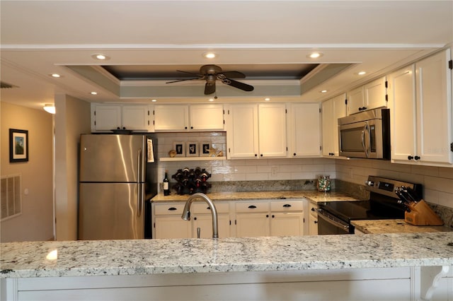 kitchen featuring visible vents, a raised ceiling, light stone counters, stainless steel appliances, and a sink