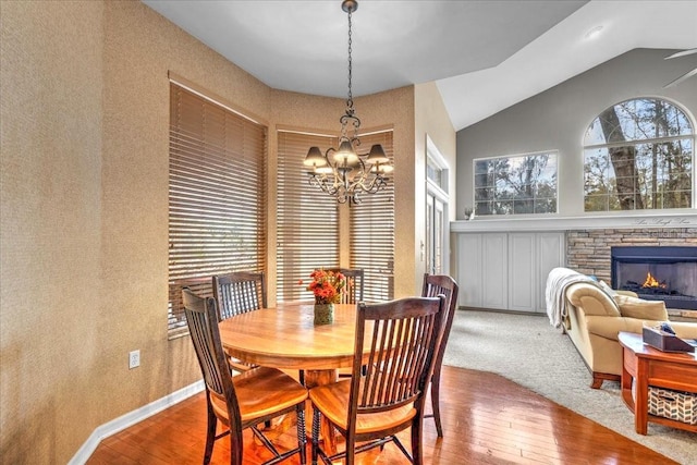 dining room with a chandelier, vaulted ceiling, hardwood / wood-style floors, and a stone fireplace