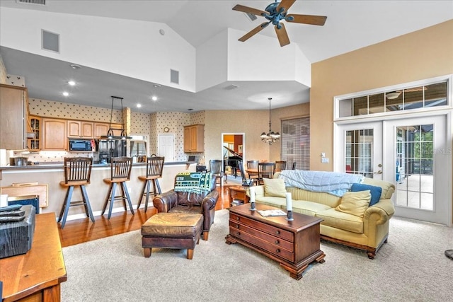 living room featuring ceiling fan with notable chandelier, high vaulted ceiling, visible vents, and wallpapered walls