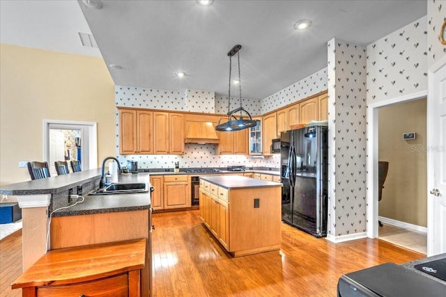 kitchen featuring dark countertops, a kitchen island, a sink, black appliances, and wallpapered walls