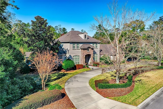 view of front of property with driveway, stone siding, a front lawn, and stucco siding