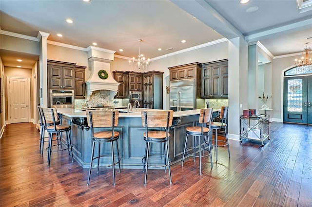 kitchen with built in appliances, premium range hood, dark wood-type flooring, a large island, and an inviting chandelier